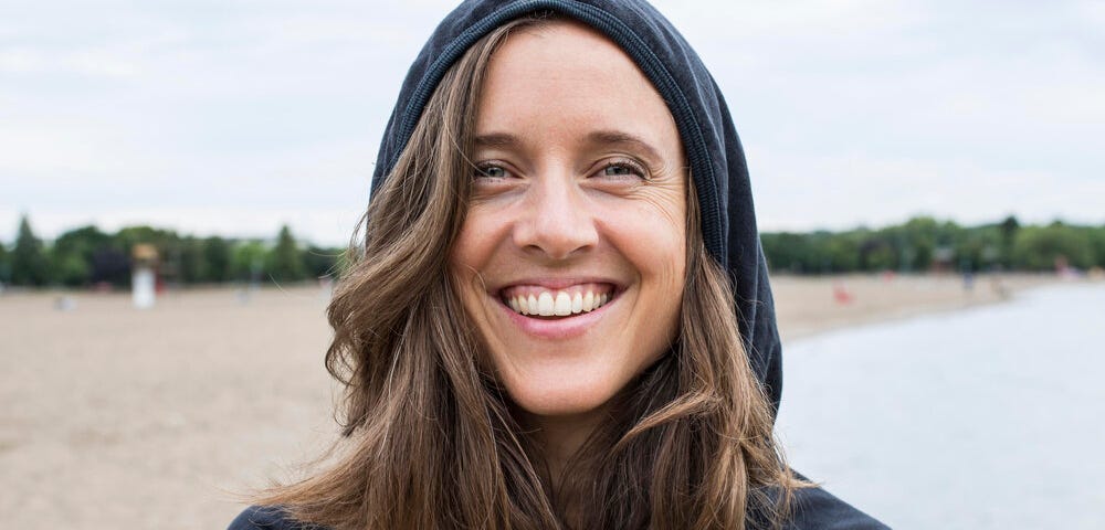 Photo of the interview subject, Jo-Anne McArthur, smiling widely on a beach, wearing a navy hoodie