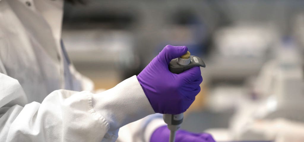 A photo of Xinhua Yan working at a lab in Cambridge. She is wearing purple gloves and pipetting.