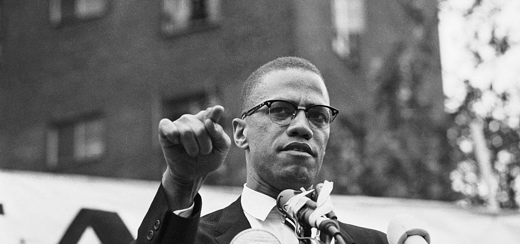 An archival black and white photo of Malcolm X giving a speech.