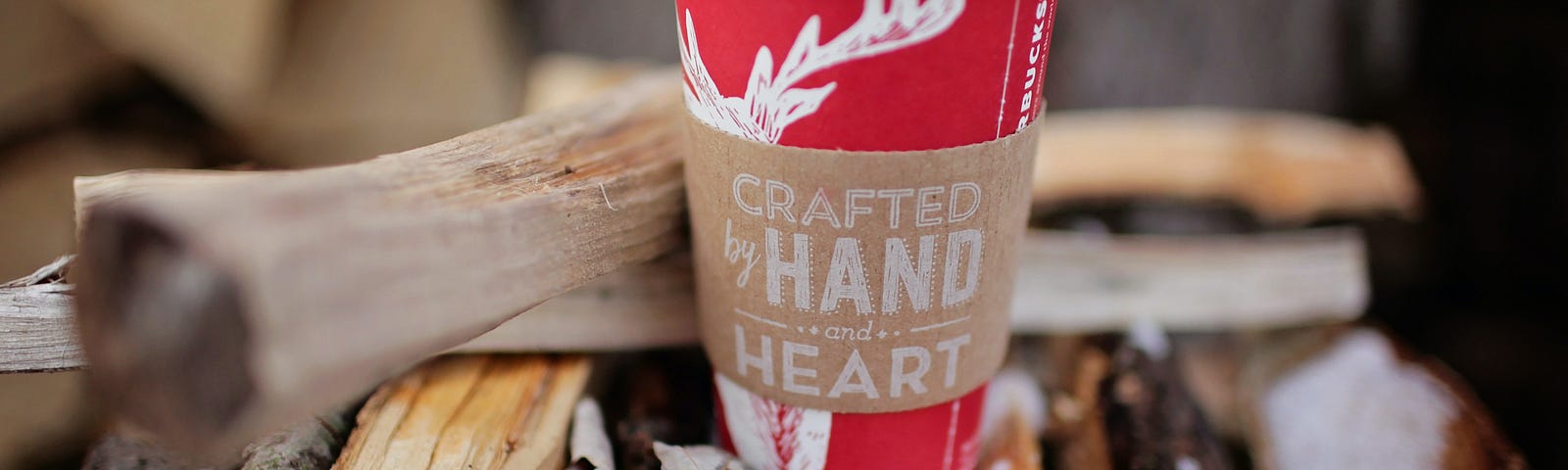 A red Starbucks cup sits on snowy branches. The coffee sleeve reads “Crafted by Hand and Heart.”