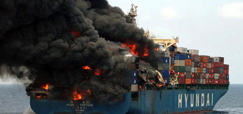 The container ship Hyundai Fortune on fire with dark pillows of smoke.