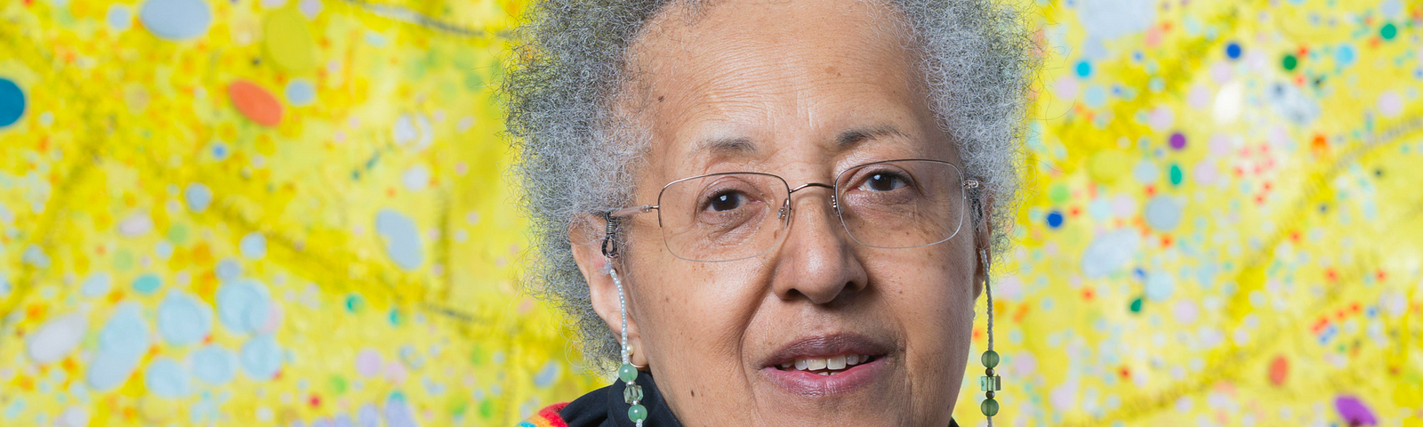 A portrait of Howardena Pindell in front of a colorful art piece.