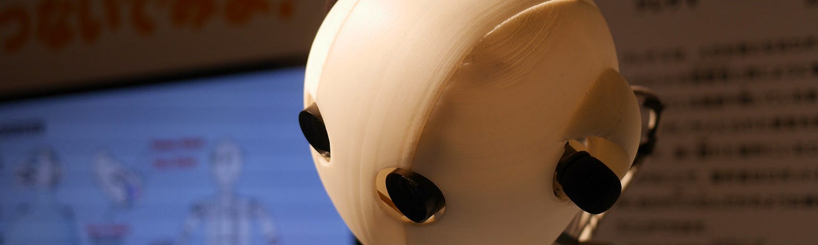 The simple, white, round head of a robot with an exhibit behind it.