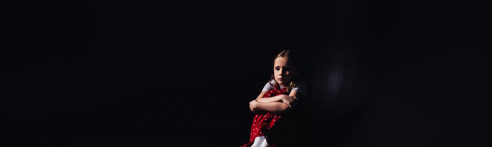 A dark photo of a young girl sitting in darkness.