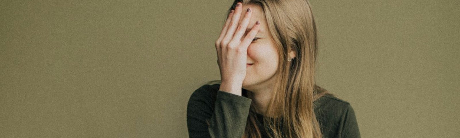 A woman sitting on the ground covering her face with her hand in embarrassment.