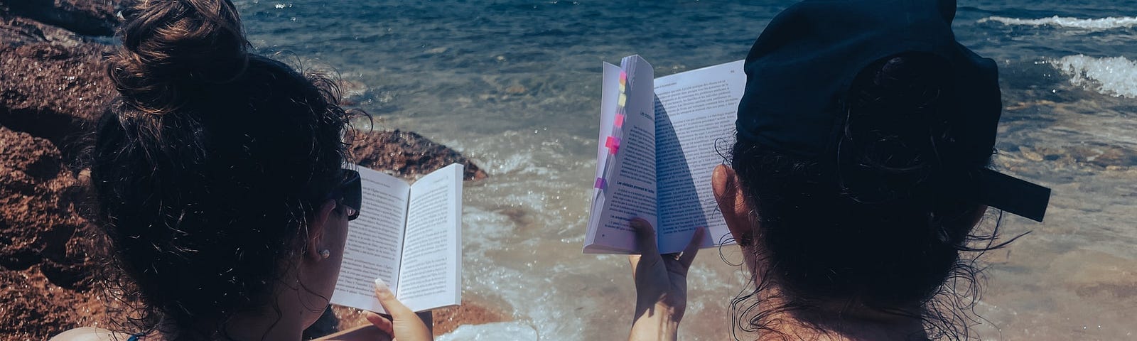 checklist two girls reading on beach in swimsuits holding books up can see water and sand its a clear day