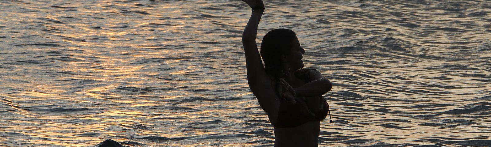 Women silhouetted in water in flamenco pose at sundown.