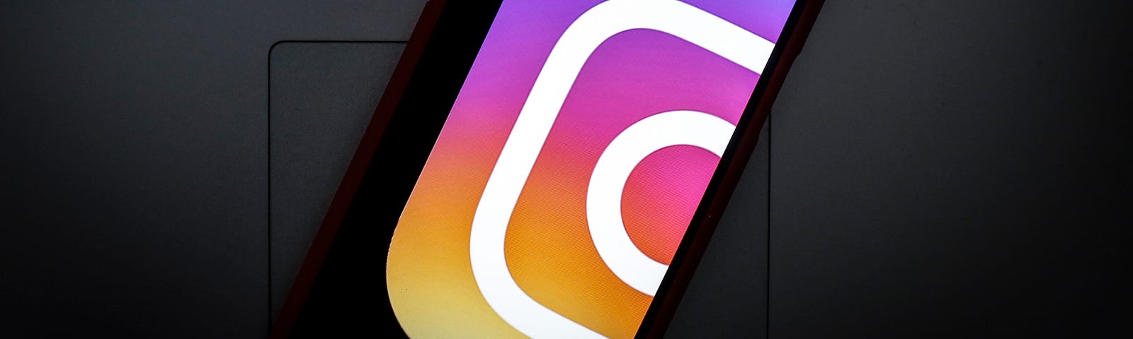 A partial Instagram logo is seen displayed on a smartphone. The smartphone is on top of a laptop keyboard.