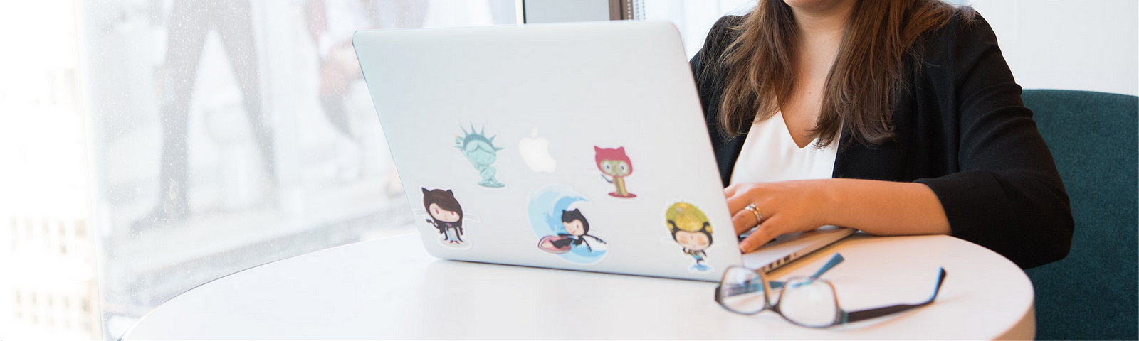 Photo of a woman typing on a laptop with 5 different GitHub octocat stickers