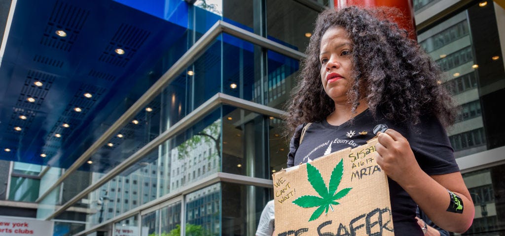 Woman holds a sign during a rally that says “[Marijuana leaf] is safer than NYPD.”