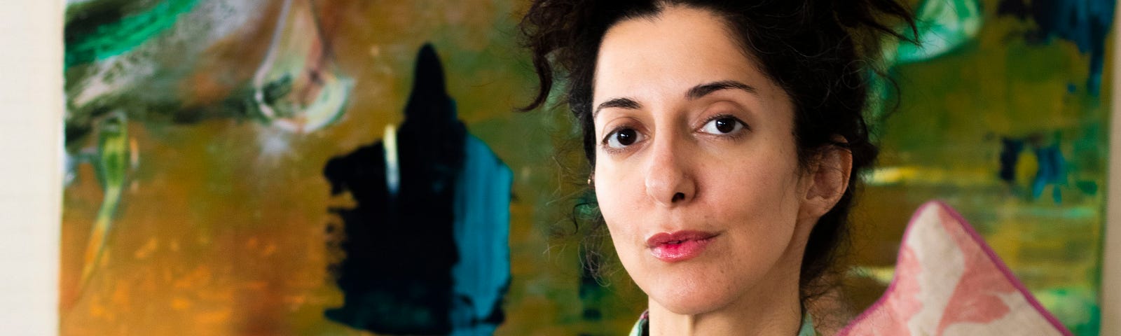 A portrait image of Porochista Khakpour sitting on a couch with her hand on a cane.