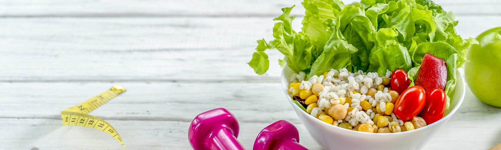 Two .5 kg dumbbells, measuring tape, and a salad on a rustic wooden table.