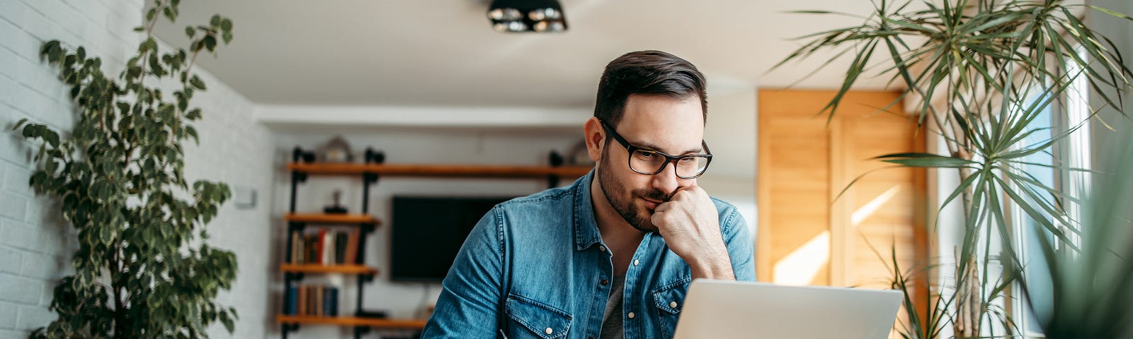 A photo of a man working on his computer at home as he is taking notes.