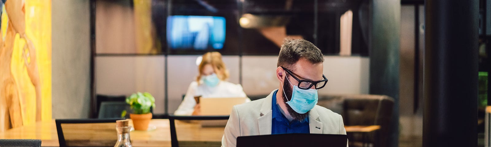 Businesspeople wearing masks in the office and sitting at further distances.