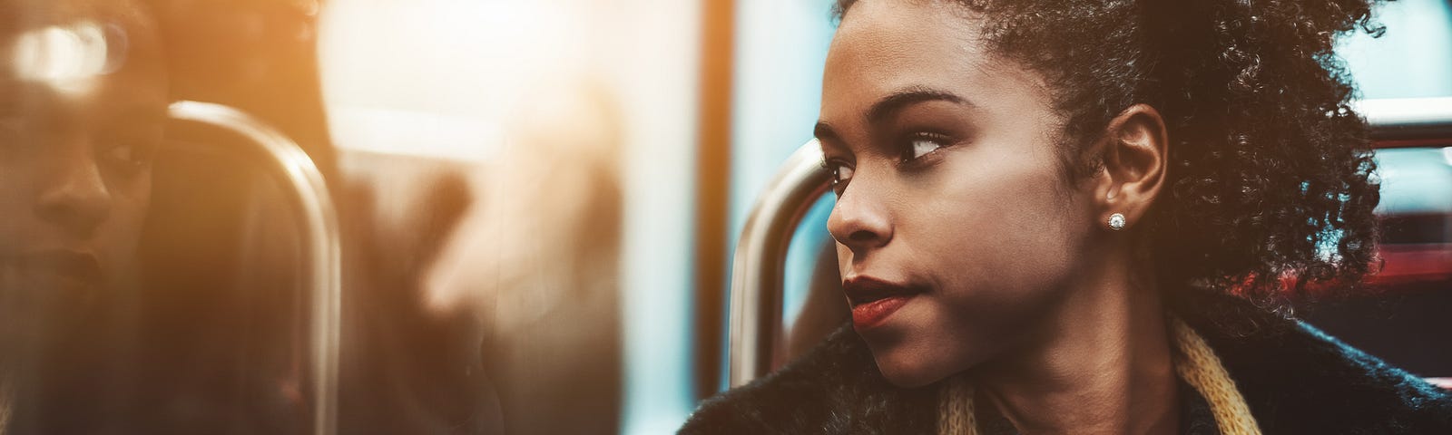 A pensive black woman looks out the window of a bus.