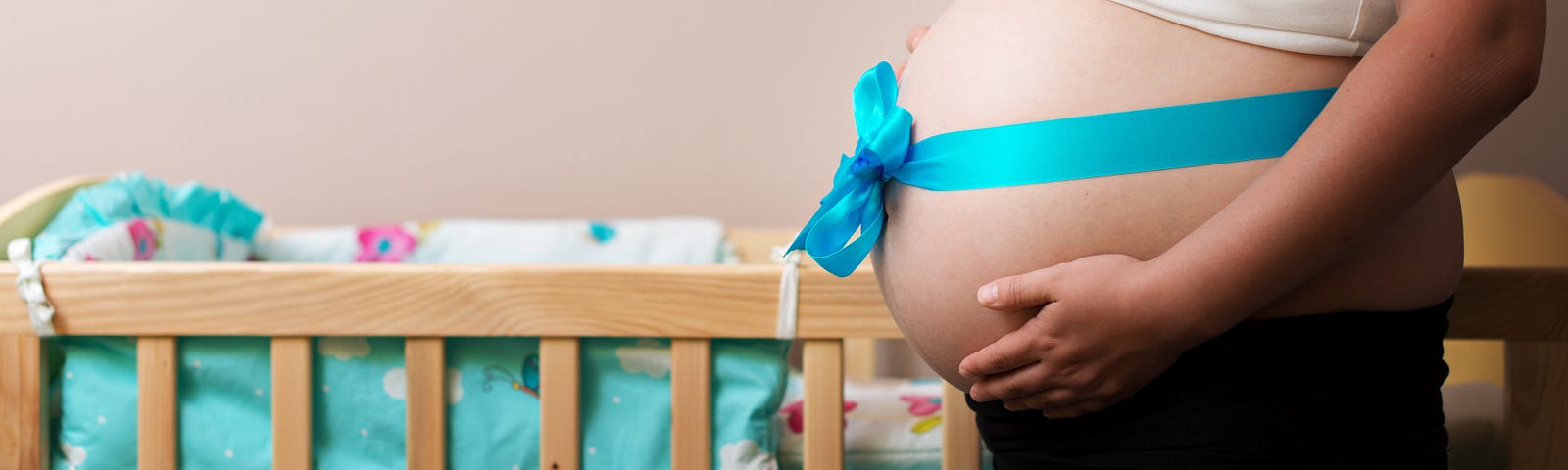 Pregnant belly wrapped in ribbon with a bow, in front of empty cot