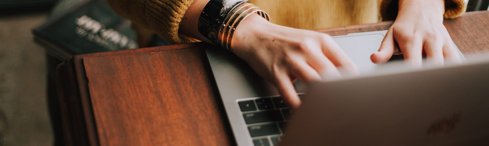 Person wearing an orange sweather typing on laptop