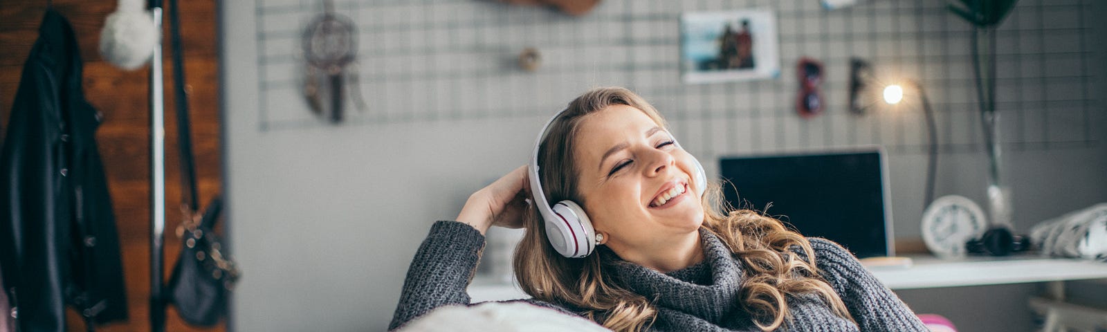 A woman holds her phone and smiles as she listens to a podcast on her headphones.