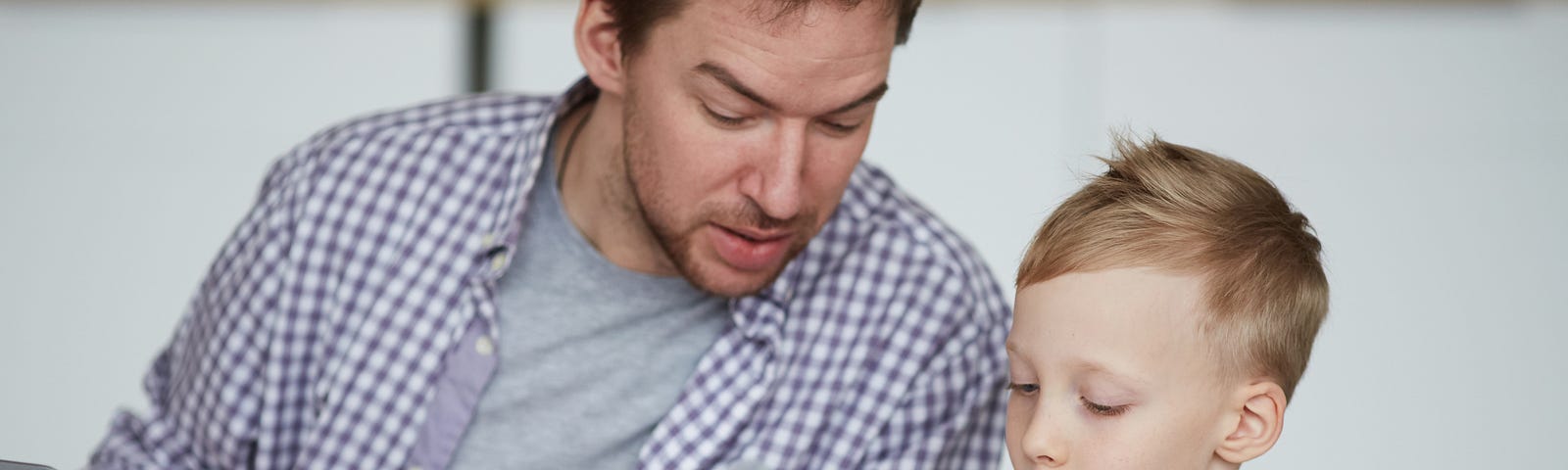 A father looks over from his laptop at his son’s school work at home.