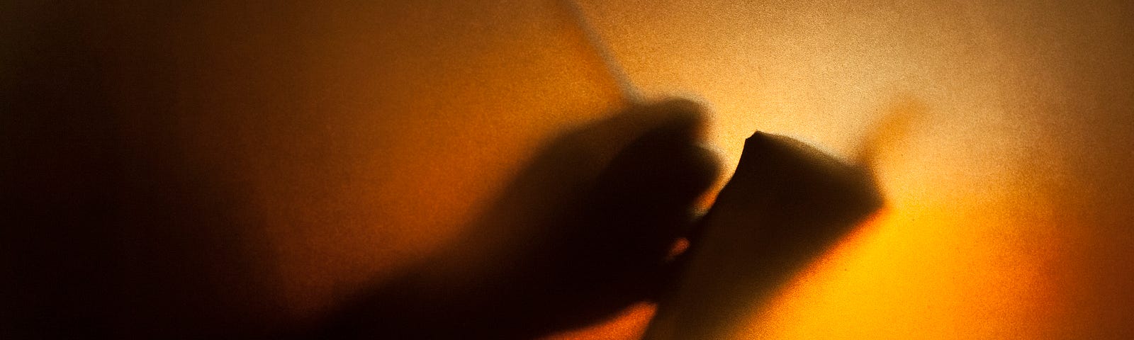 Silhouette of man writing on book behind textured glass.