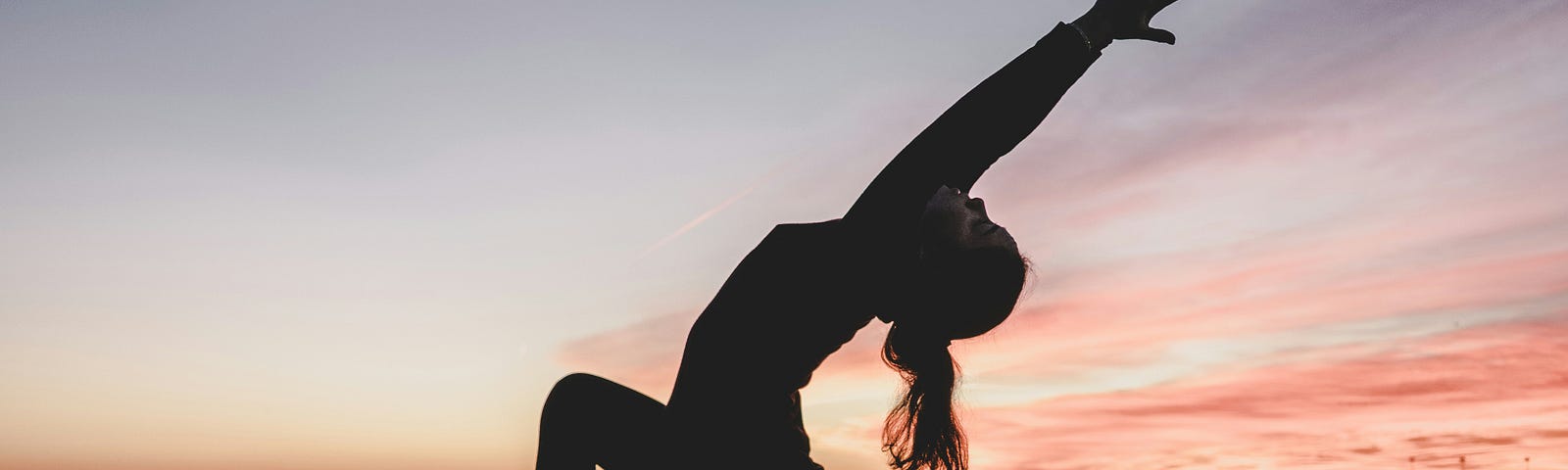 A silhouette of a woman in a deep stretching yoga moves during sunrise at the beach.