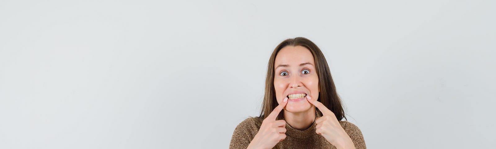 Young woman forcing her mouth into a smile using her fingers. She doesn’t appear to smiling, she knows she is being forced.