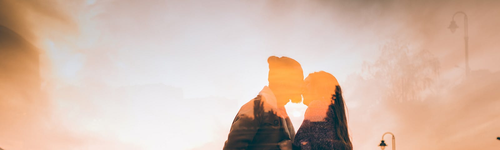 Double exposure orange-filtered photo of a couple kissing against bright sky.