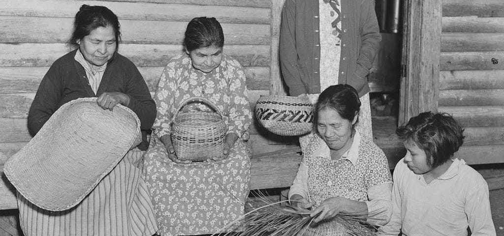 A black and white vintage photo of Choctaw women weaving baskets in the early to mid 20th century.