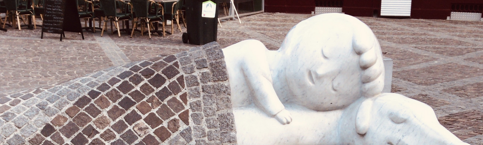 Reclining white statues of larger than life-size child and dog sleeping, with the paved ground as bedcovers.