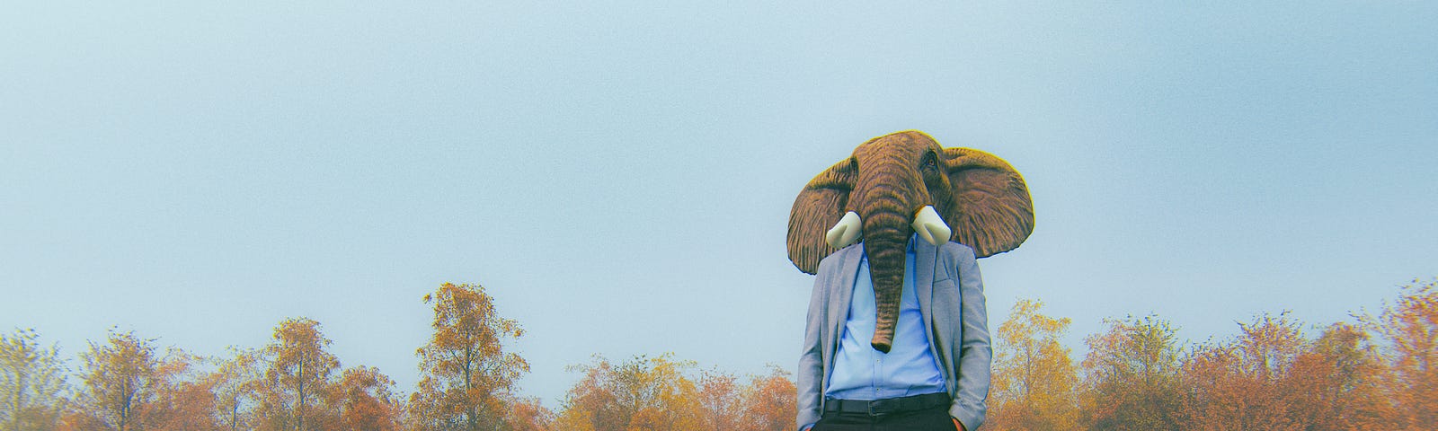 A photo of a man with an elephant face standing in a field with a briefcase next to him.