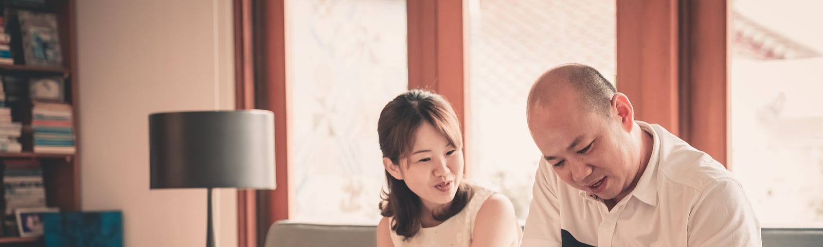 A couple sits on a couch in front of a laptop while one person writes in their notebook.