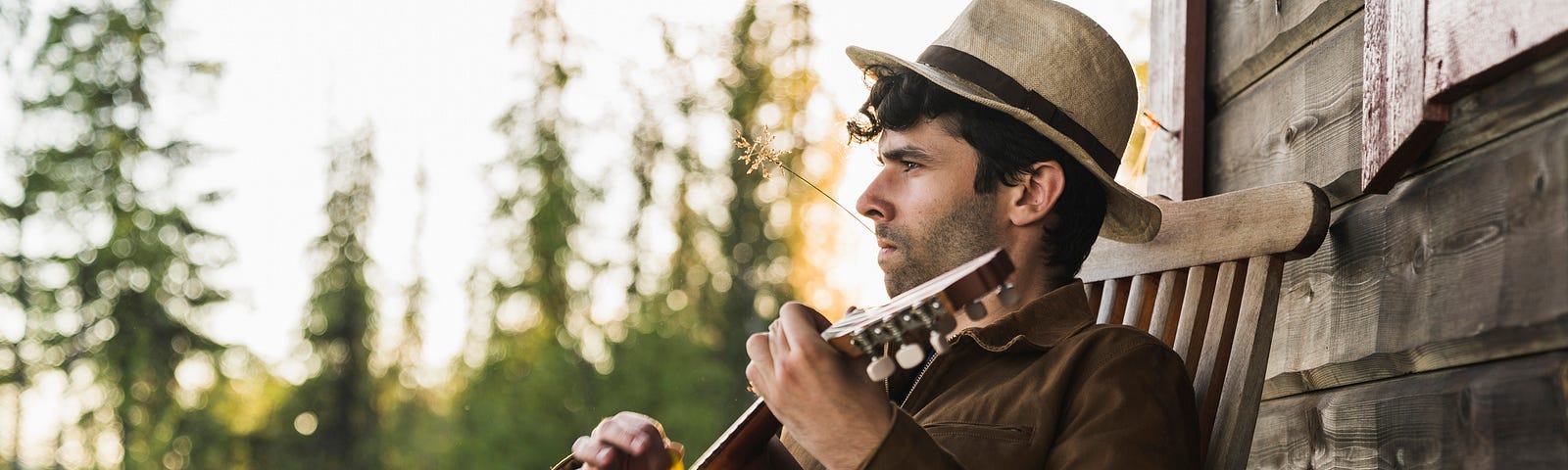 Young man sitting on veranda of a wood house, playing the ukulele.