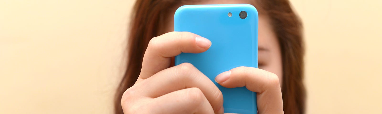 Close up of a teenager using her smartphone. Her face is obscured by her phone.