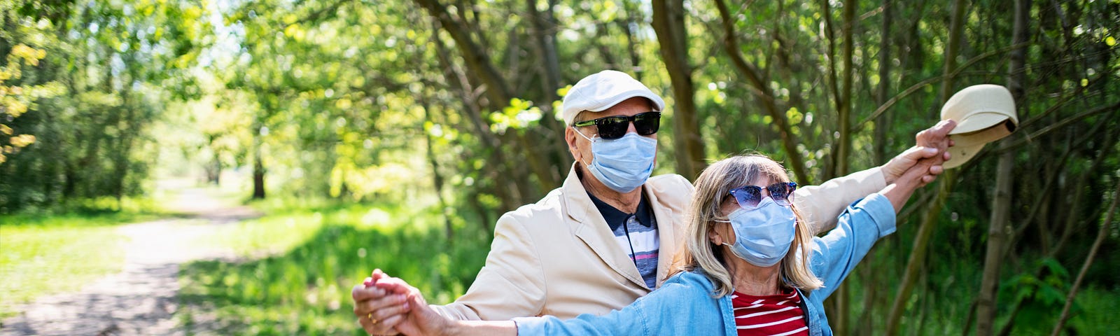 A senior couple walking joyfully through the park wearing masks