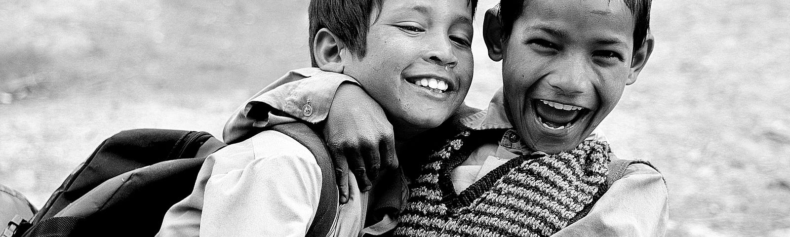 Black and white photo of two happy young boys from the waist up, one with his arm around the other’s neck.