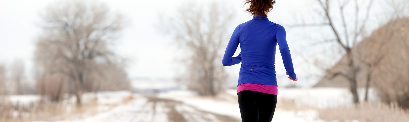 A person running on a snowy dirt road away from the camera.