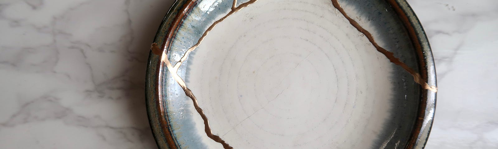 A white and grey bowl repaired together with gold streaks across the surface