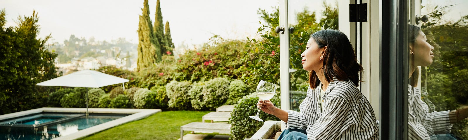 Smiling woman enjoying glass of wine while watching sunset from backyard.