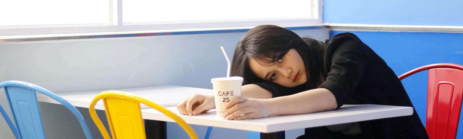 A woman is leaning against a table while holding a cup of coffee.