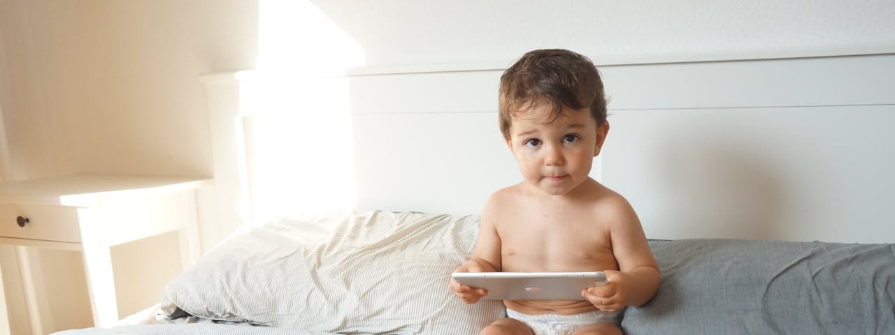 Child Sitting on a Bed Using a Tablet.