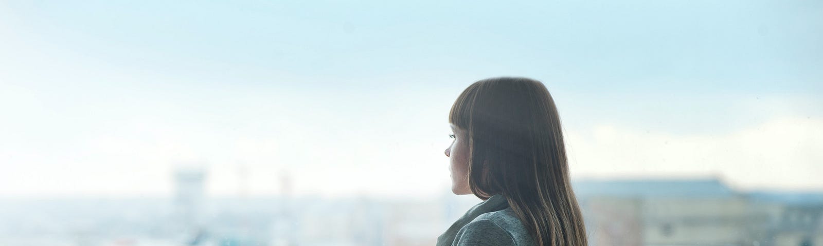 A young woman in profile, gazing out the airport’s large window at the planes outside.