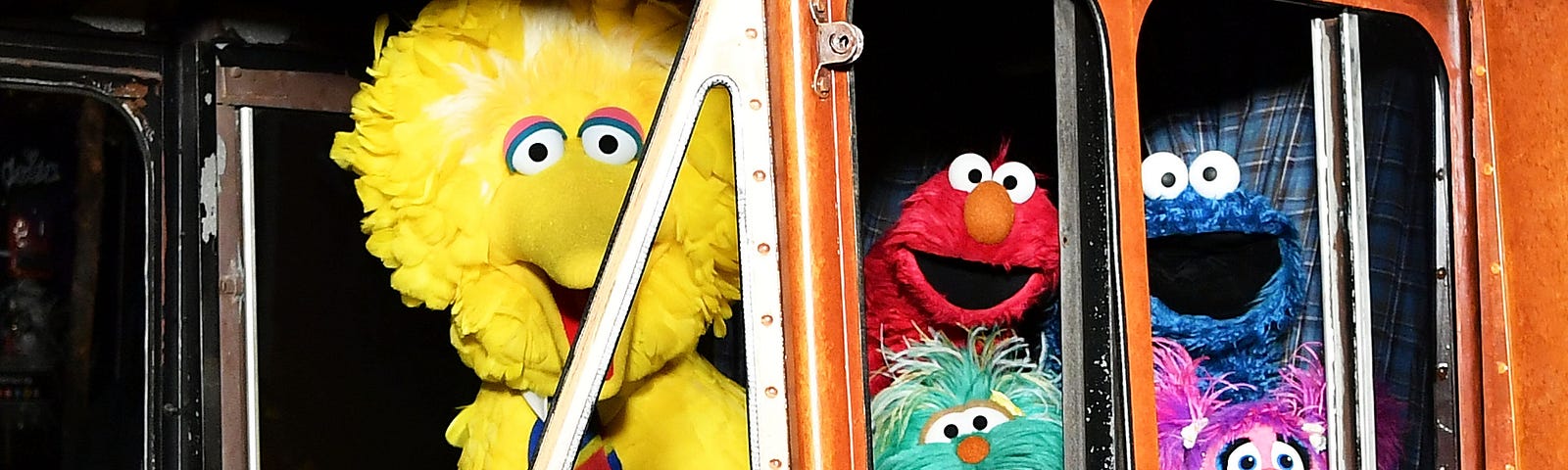 Sesame Street characters Big Bird, Elmo, Cookie Monster, and Abby Cadabby inside a bus.