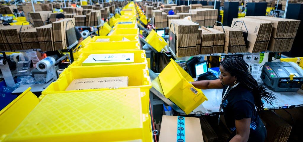 A photo of a woman in an Amazon factory putting packages on the queue line.