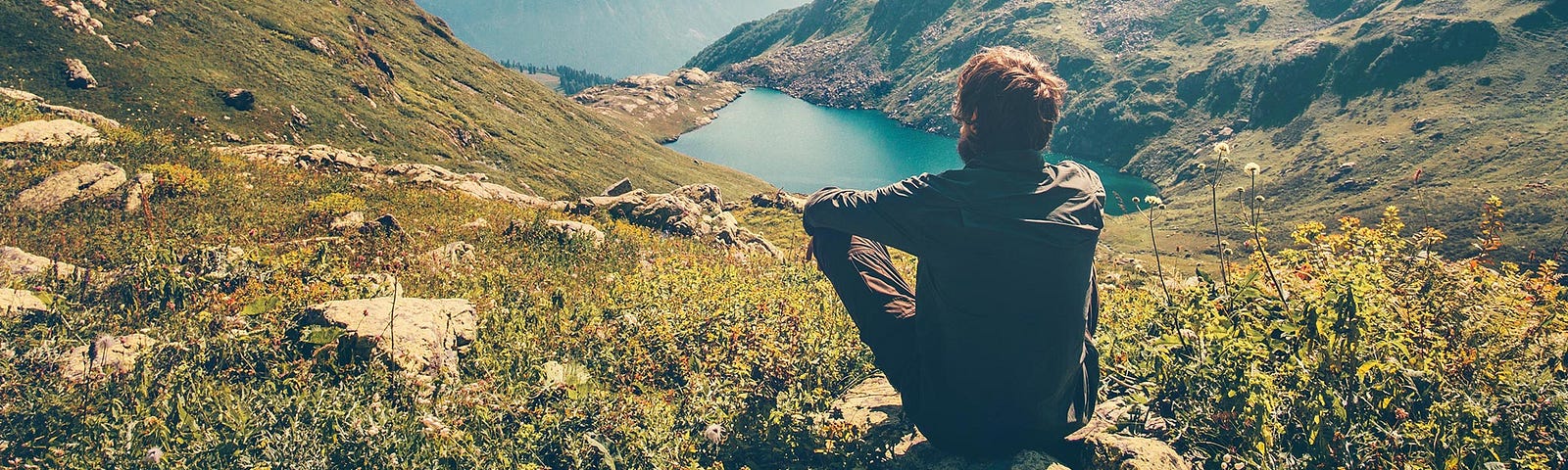 Silent man sitting on a mountainside looking at a lake
