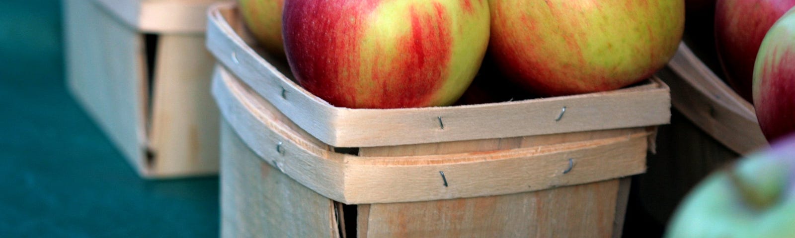 Red apples in small wooden baskets for sale at a farmers market.