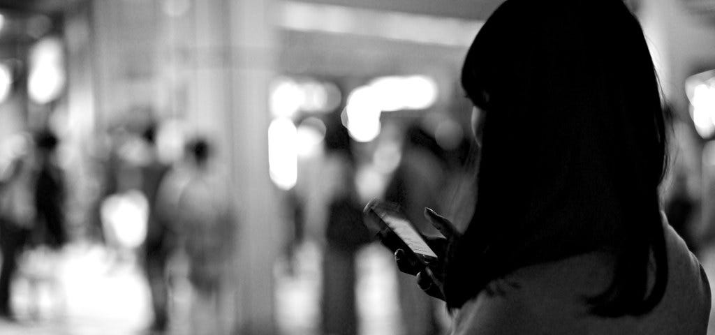 A black and white photo of a black-haired woman on her phone in a busy city street.