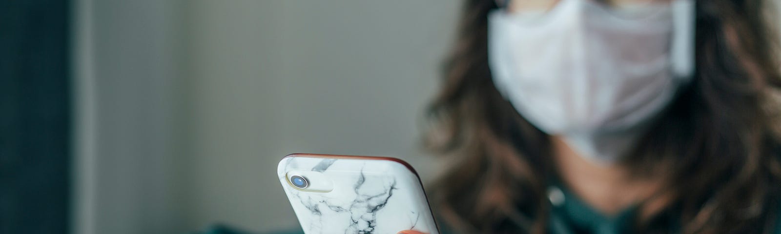 A person wearing a face mask, using their phone. They seem to have an optimistic expression.