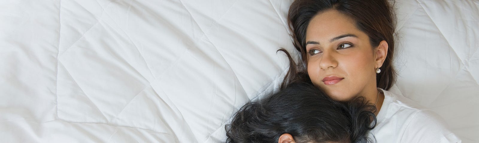 Tired South Asian mother holding her sleeping daughter.