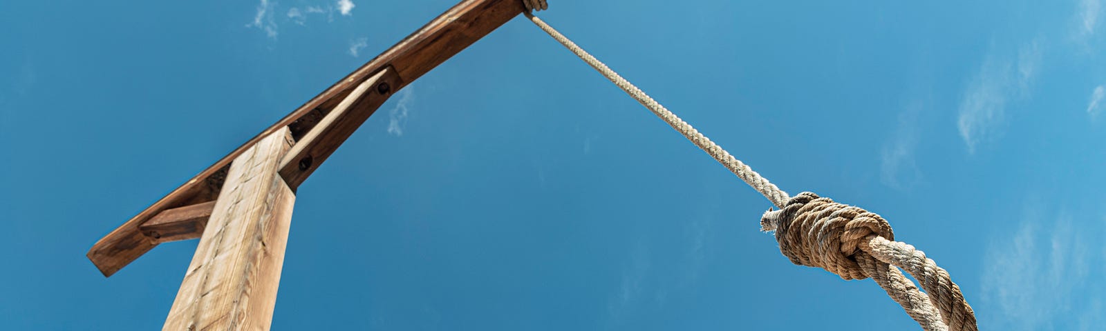 Bright blue sky with scaffold and noose in foreground.