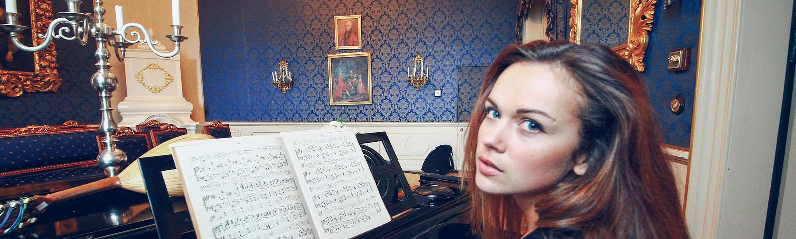 A woman in black longsleeves playing piano while looking over her shoulder.